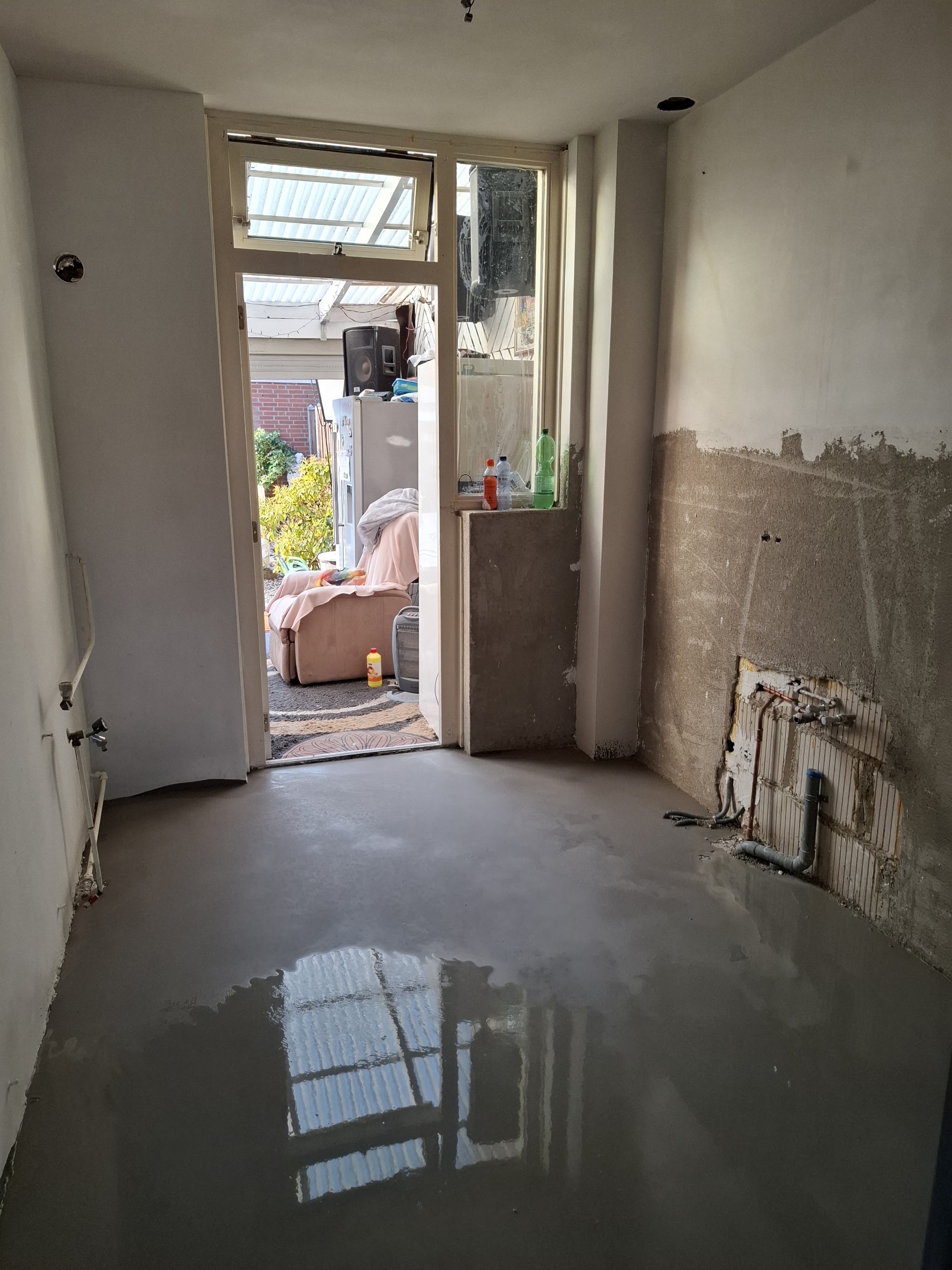 Gang met vers gestorte vloer en voorbereide wanden tijdens een renovatie