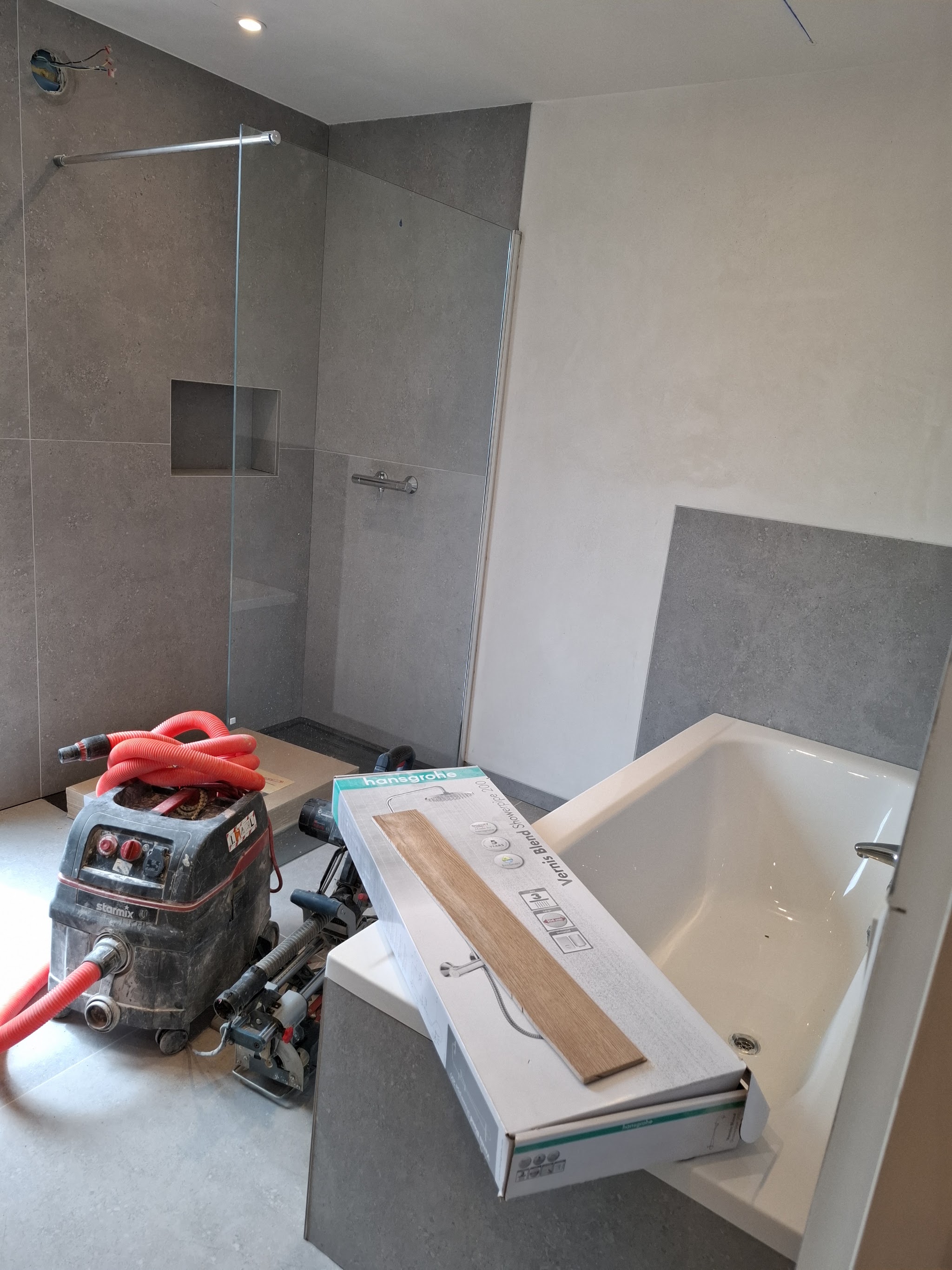 Badkamer in aanbouw met grijze tegels en bad